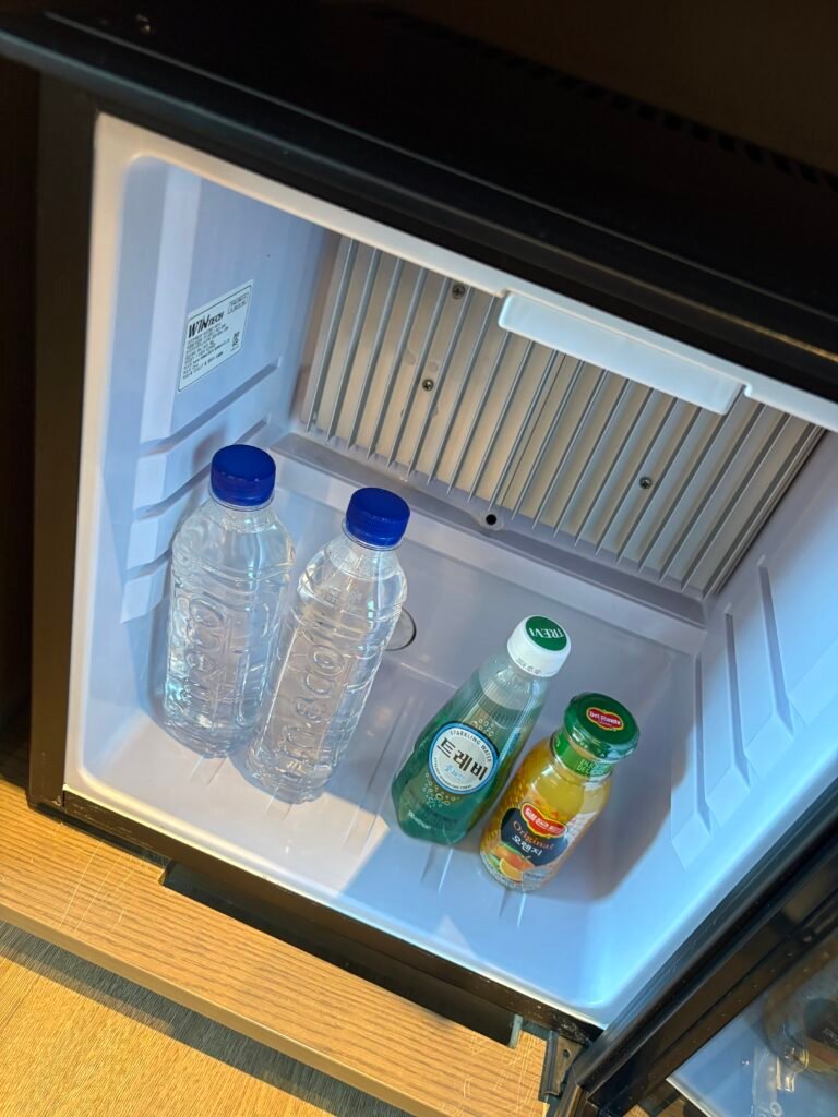 Open minibar refrigerator with complimentary bottled water and soft drinks